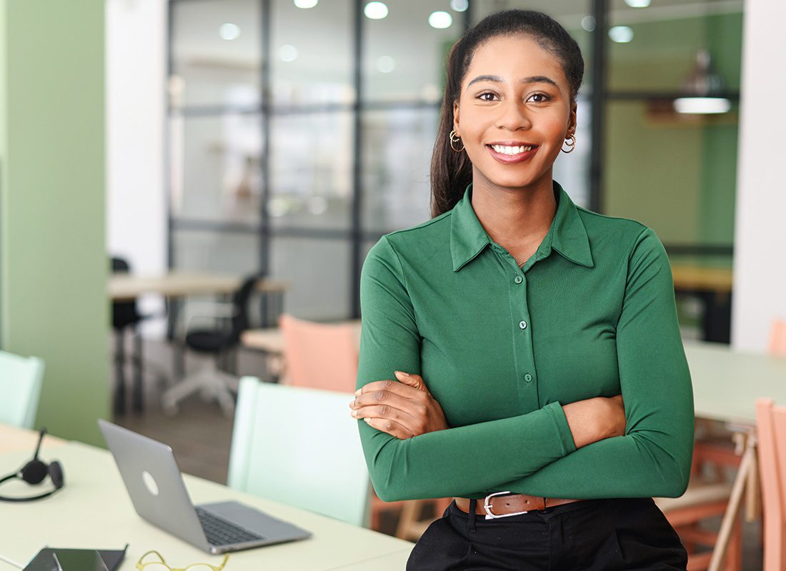 About Our Agency - Friendly Business Woman Standing by Her Desk Wearing a Green Shirt